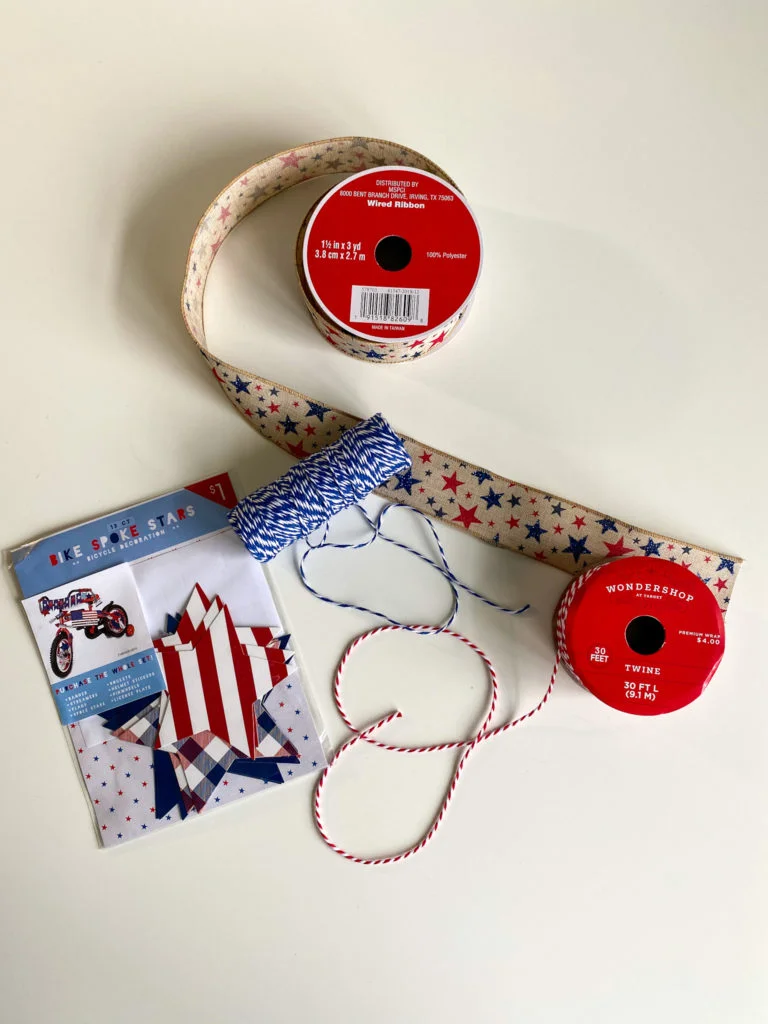 spool of burlap ribbon with red and blue stars, blue and white twine, red and white twine, and pack of red/white/blue paper stars