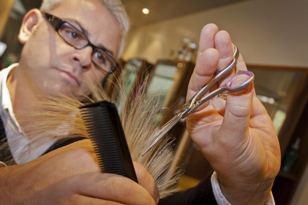 Male hair stylist cutting hair with scissors and comb