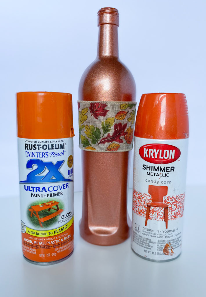 Cans of Rust-Oleum Gloss Real Orange spray paint and Krylon Candy Corn Shimmer Metallic spray paint with finished glass bottle in middle