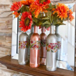 Two caramel latte bottles and one candy corn painted bottle filled with burlap ribbon and rust colored sunflowers, displayed on a mantel in front of mirror