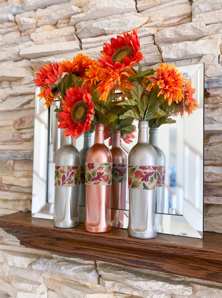 3 fall bottles on fireplace mantle in front of mirror, filled with rust sunflowers and mums