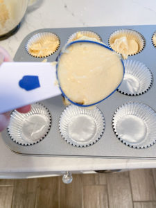 Wilton cupcake scoop filled almost to top with batter, in front of cupcake pan filled with foil cupcake liners