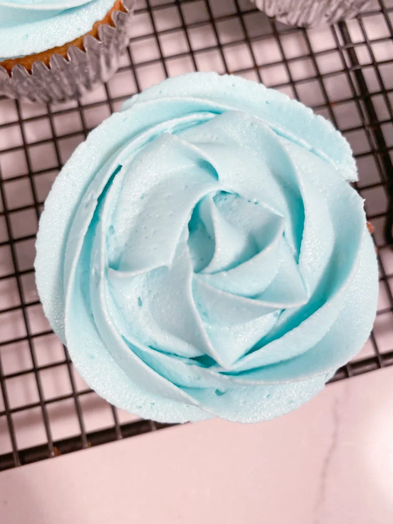 Cupcake decorated with blue rosette icing on a cooling rack