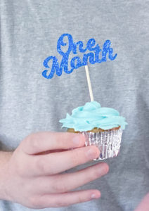 Cupcake with blue icing rose and a blue glitter cupcake topper that reads "One Month"