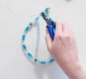 Crimping tool being used to crimp bead on finished beaded chain with seaglass colored beads