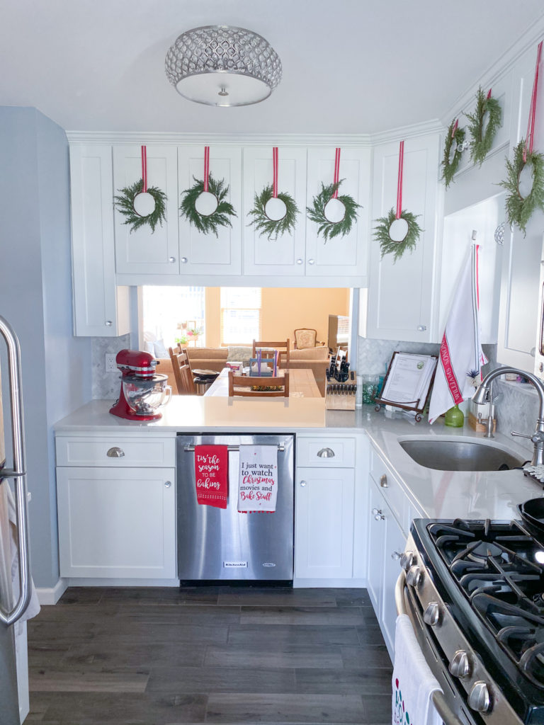 White kitchen cabinets with green wreaths hung with red and white ribbon on upper cabinets, full vertical view of kitchen