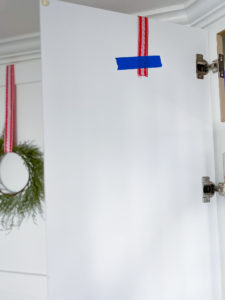 Back of white cabinet door with red and white ribbon secured with strip of blue painter's tape a few inches down from the top.