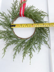 Measuring tape showing inner diameter of 4.5 inches of green wreath with red, white & silver ribbon on white cabinet door