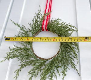 Measuring tape showing outer diameter of 11 inches on green wreath hung with red, white & silver ribbon on white cabinet door