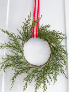Closeup of green wreath on white cabinet door hung with red, white & silver ribbon