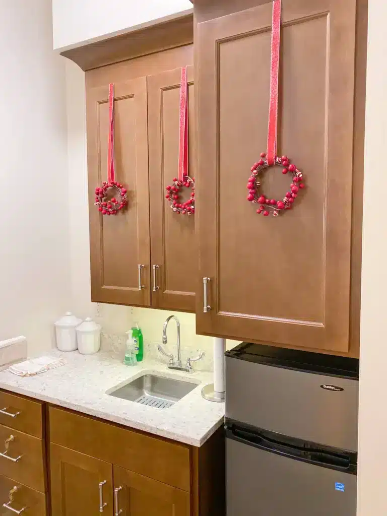 3 Red and white candy Christmas garland hanging on red glitter ribbon on brown kitchen cabinets.