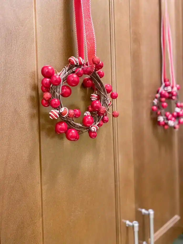 Coiled garland of red berries with red and white candy on red and white glitter ribbon as Christmas wreaths on brown wood kitchen cabinet doors