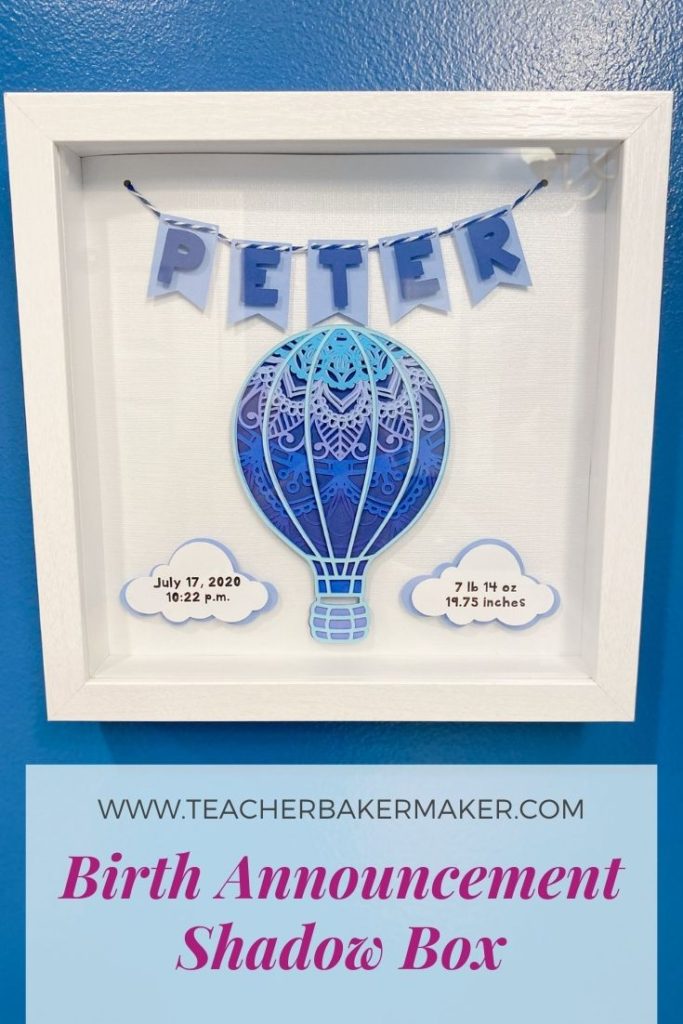 Pinterest Image of Birth Announcement Shadow Box Mandala of hot air balloon in shades of blue with vital stats on clouds and name spelled out on pennant banner, hung on blue wall