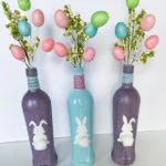 Easter Decorations Ideas spray painted glass bottles two multicolor glitter purple one gloss blue with bunny decals with cotton ball tails pastel twine Easter egg sprays