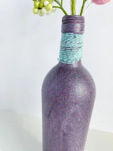 Multicolor Purple Glitter spray painted glass bottle with aqua/white twine around neck of bottle, rear view