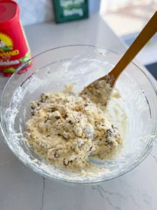 Irish soda bread batter in glass bowl with wooden spoon and container of raisins