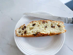 Slice of Irish soda bread on white plate with serrated bread knife