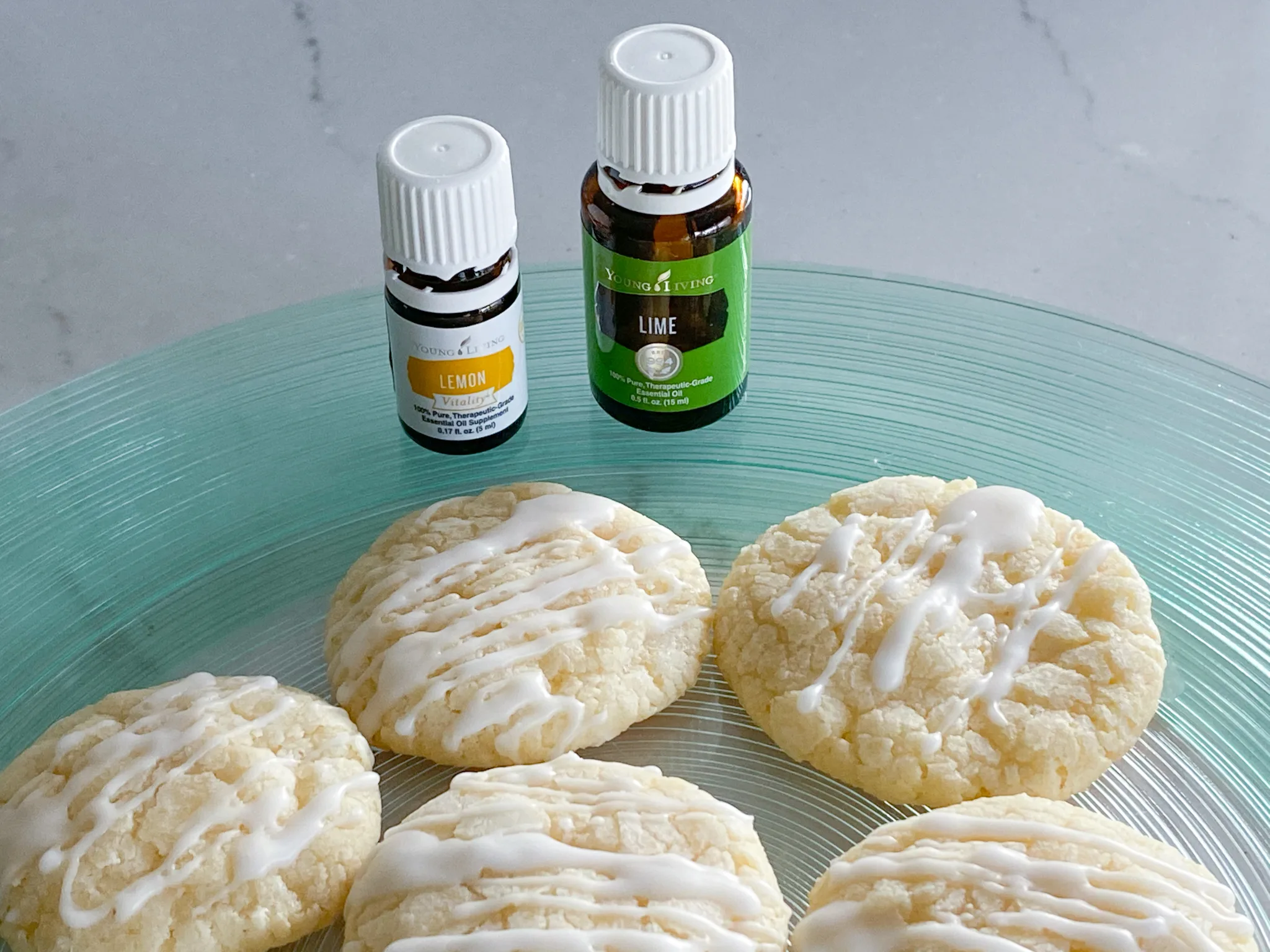 Glazed Lemon Lime cookies on blue green glass plate with bottles of Young Living brand lemon and lime essential oils