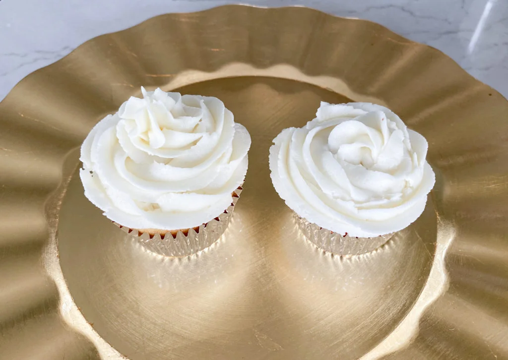 Two cupcakes with ivory buttercream on gold platter