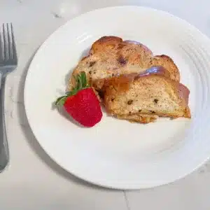 raisin challah french toast on white plate with strawberry, knife and fork