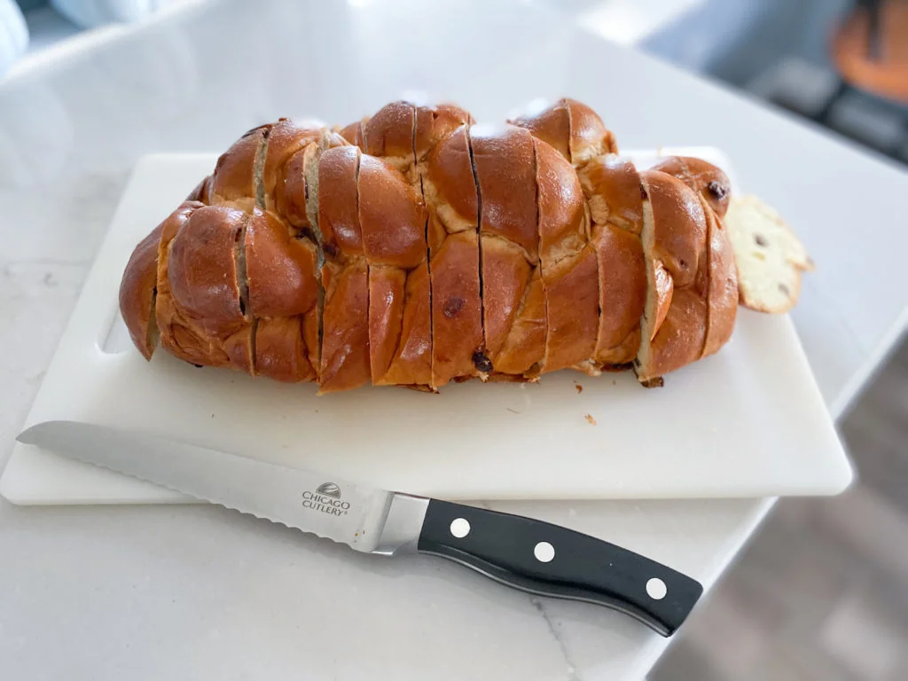 braided raisin challah bread sliced in 1 inch thick slices on white cutting board with serrated bread knife