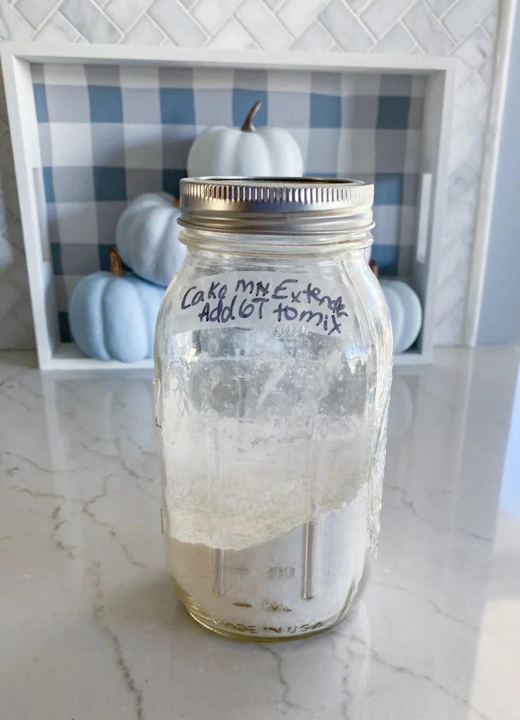 Mason jar with cake mix extender to doctor up a cake mix. Label says cake mix extender Add 6 T to mix, in front of blue ombre pumpkins in blue and white plaid tray