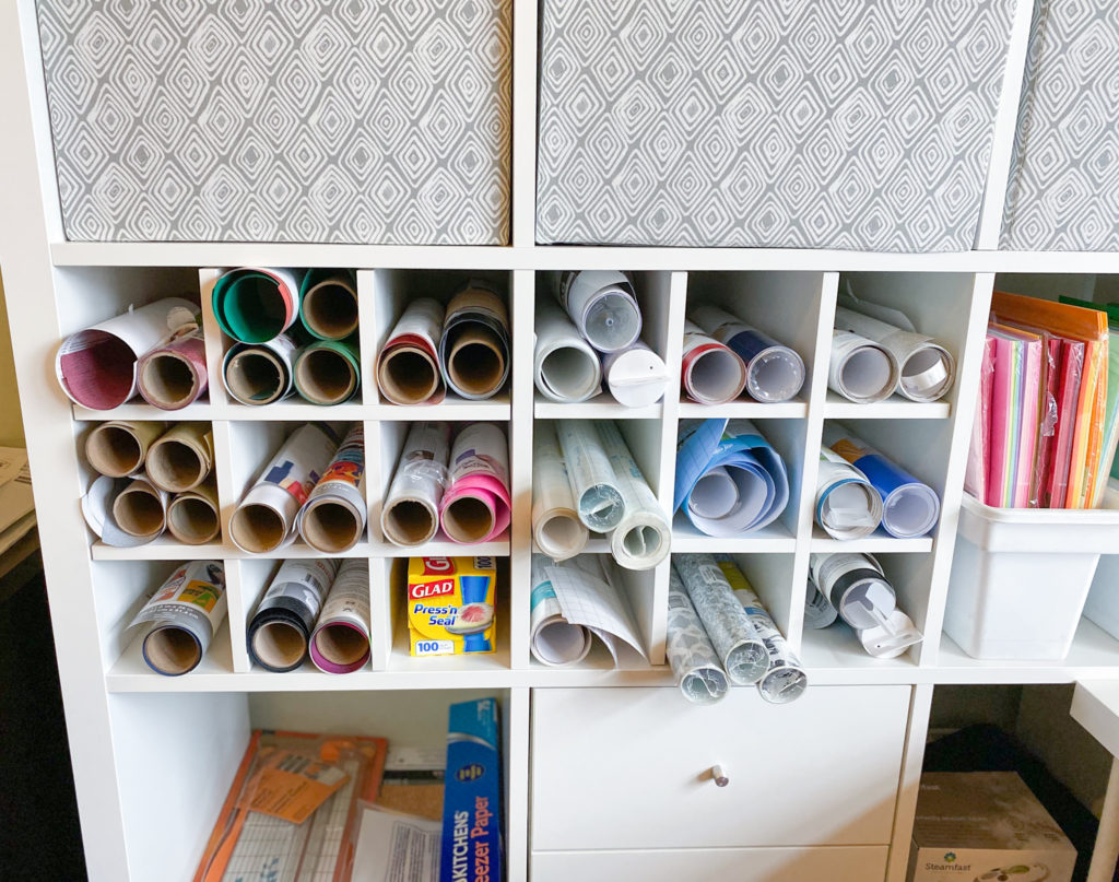 Bottle racks in 2 cubbies of Kallax craft storage unit with rolls of adhesive vinyl and HTV vinyl for Cricut supply organization