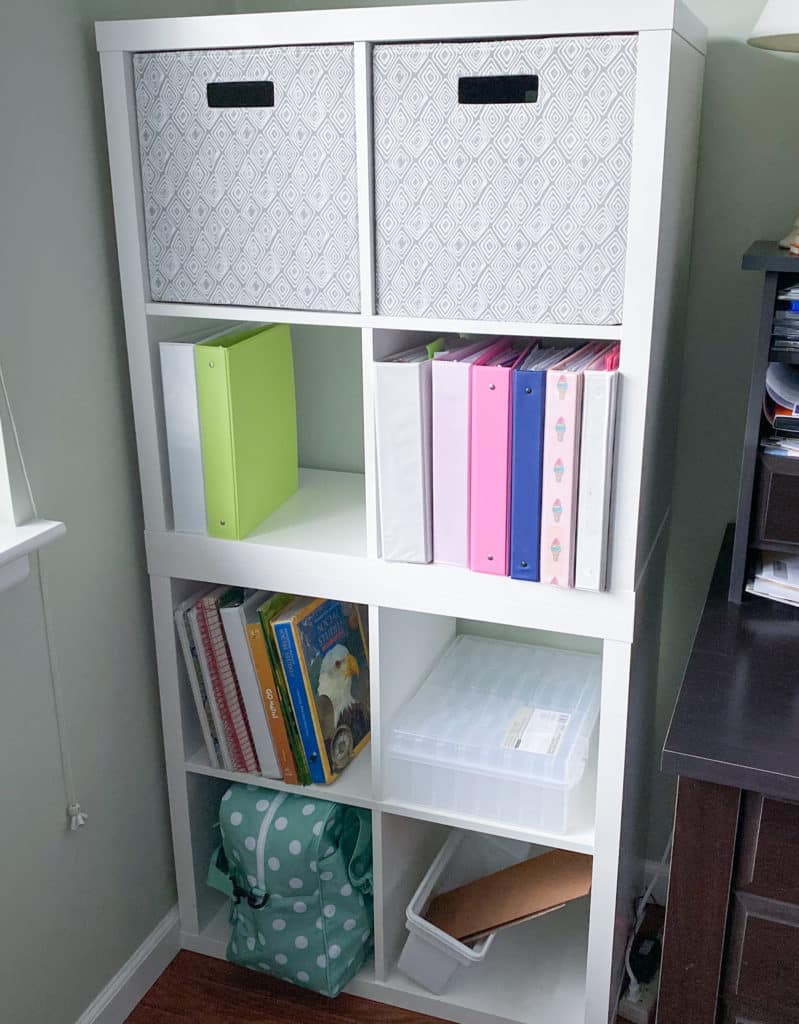Two 2x2 white Kallax storage units stacked with gray diamonds fabric bins, binders, books, and mint green sewing machine case