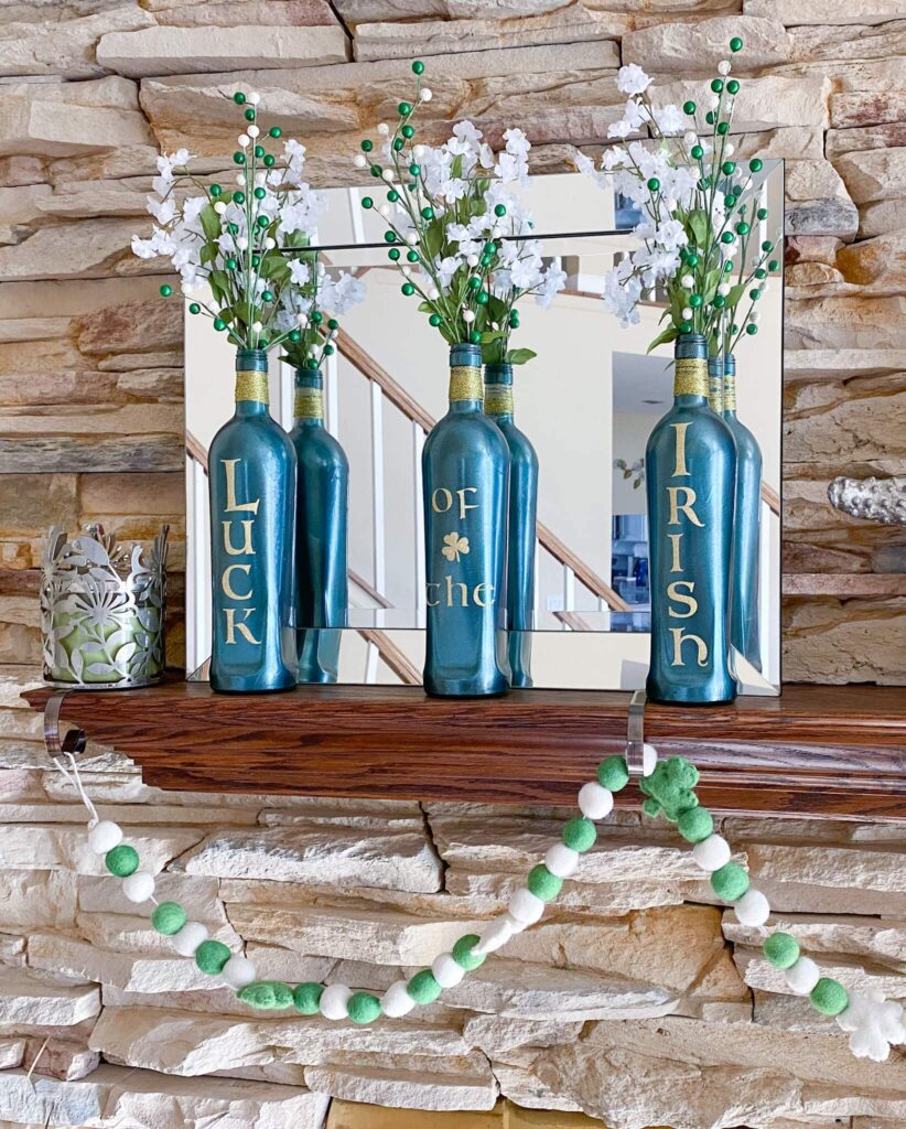 Mantel shelf with 3 green bottles with Luck of the Irish in gold letters, green/white berries, white flowers with green/white shamrock garland