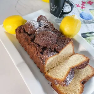 Sliced Loaf of Earl Grey Pound Cake on white platter with lemons and cup of tea