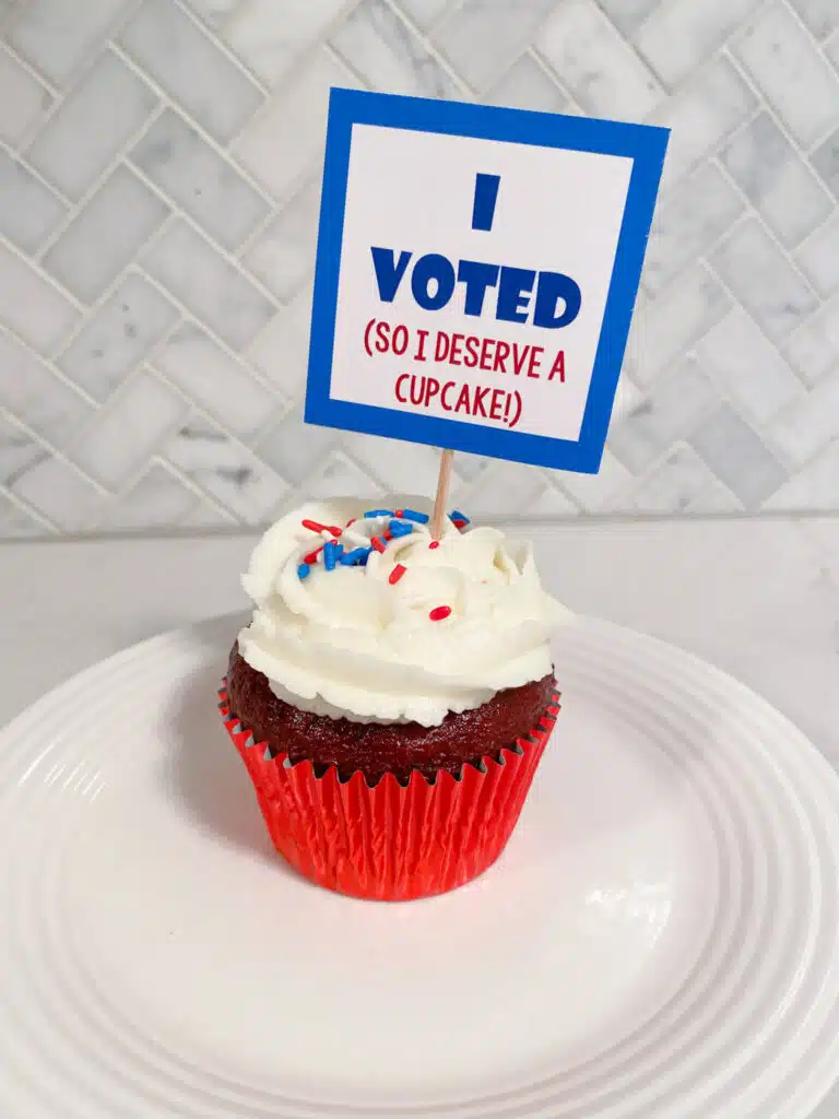 Red velvet cupake with white swirl frosting and red, white & blue sprinkles and cupcake topper that says "I Voted! (So I deserve a cupcake)