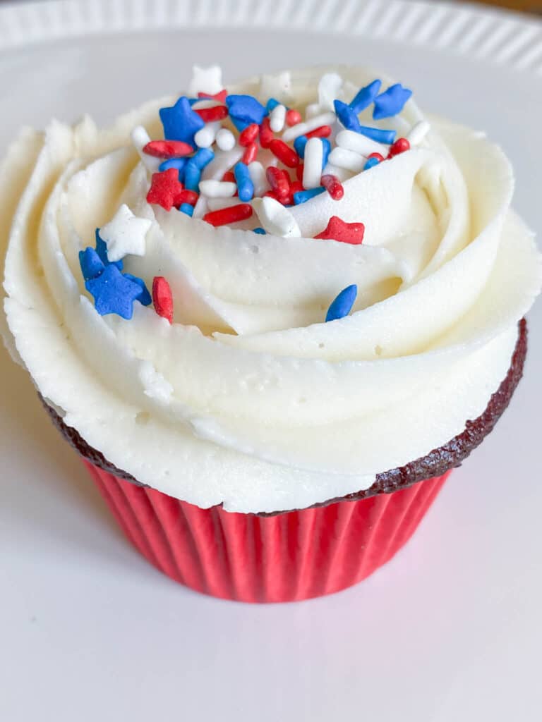 Red velvet cupcake with vanilla buttercream swirl frosting and red, white and blue sprinkles
