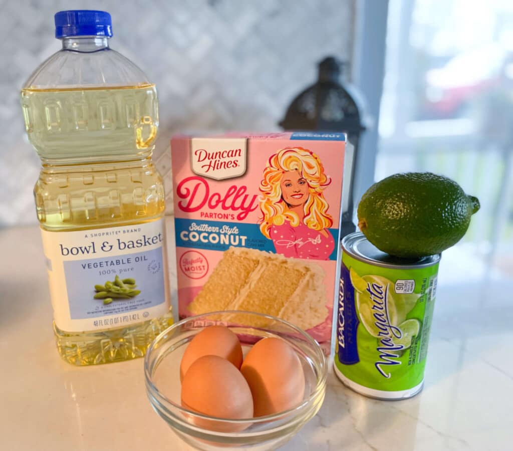 Ingredietns for lime coconut cupcakes: bottle of vegetable oil, Dolly Parton coconut cake mix package, Bacardi frozen margarita mix can, 1 lime, 3 brown eggs in class bowl