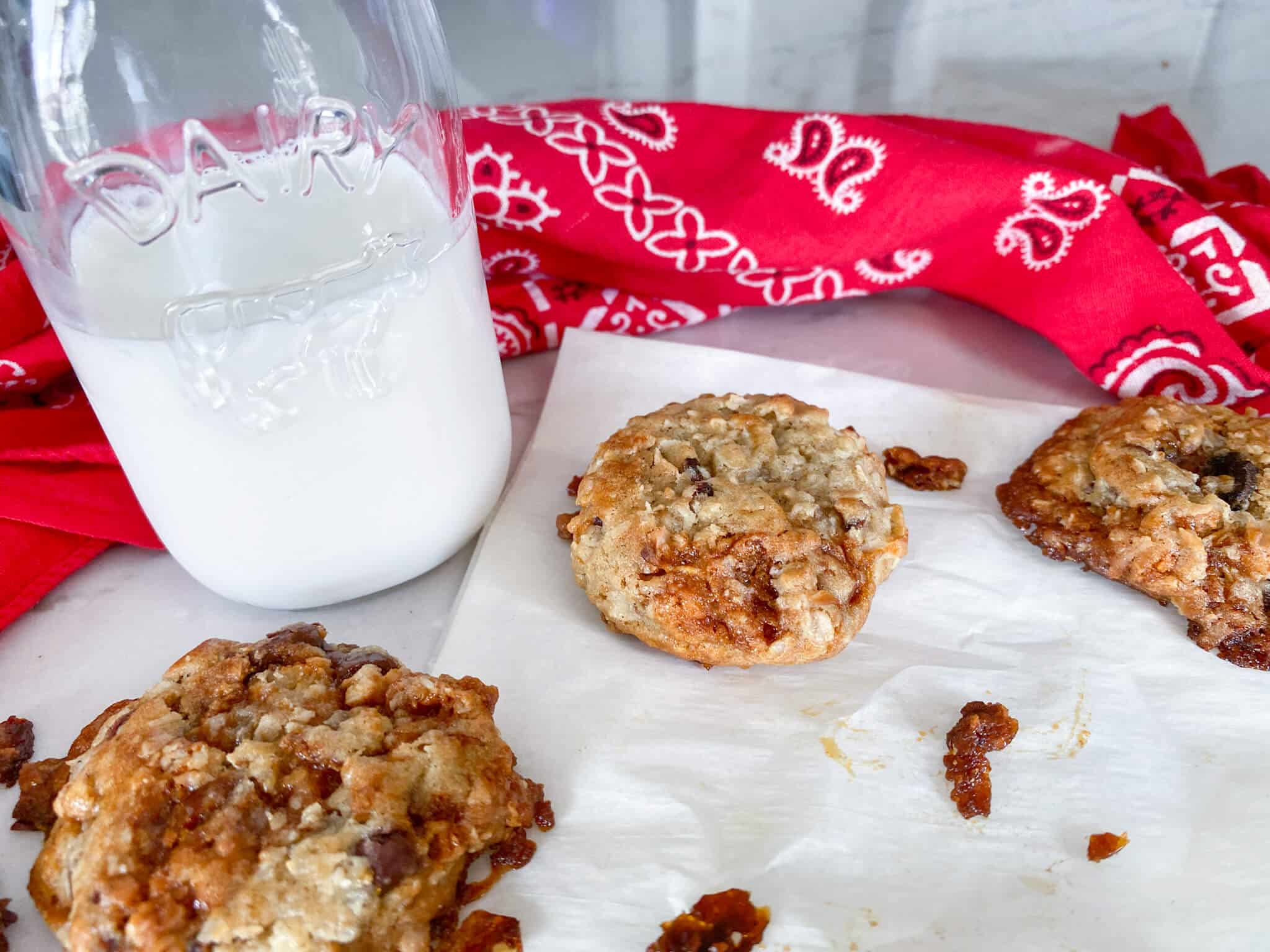 3 bacon chocolate chip cookies with glass of milk and red/white bandana on parchment
