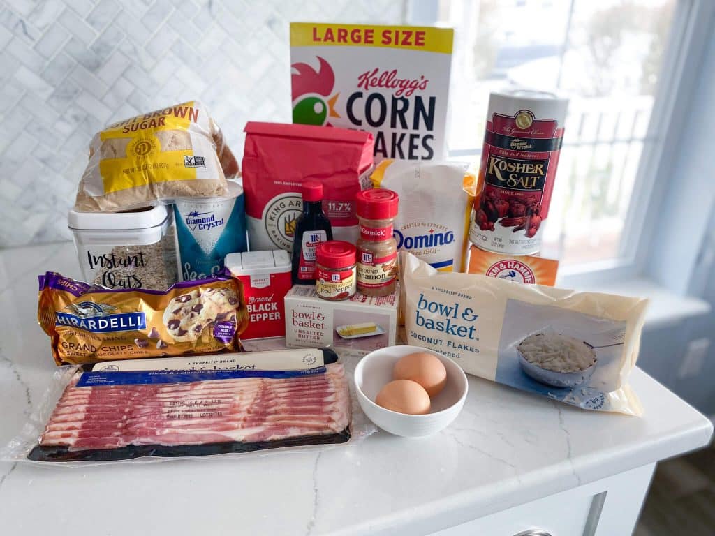 Ingredients for Cowboy cookies - brown sugar, instant oats, salt, flour, corn flakes, kosher salt, sugar, baking powder, coconut, brown eggs in small bowl, bacon, chocolate chips, black pepper, vanilla extract, cinnamon, cayenne pepper, unsalted butter