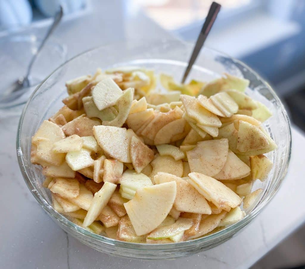 glass bowl of apple slices coated with spices and apple juice concentrate with spoon
