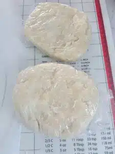 2 round discs of pie crust dough wrapped in clear plastic wrap on top of pastry mat.