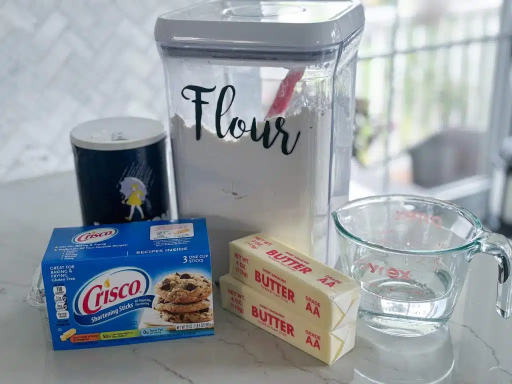 Canister of flour, container of salt, Crisco shortening sticks, 2 sticks of unsalted butter, measuring cup of ice water