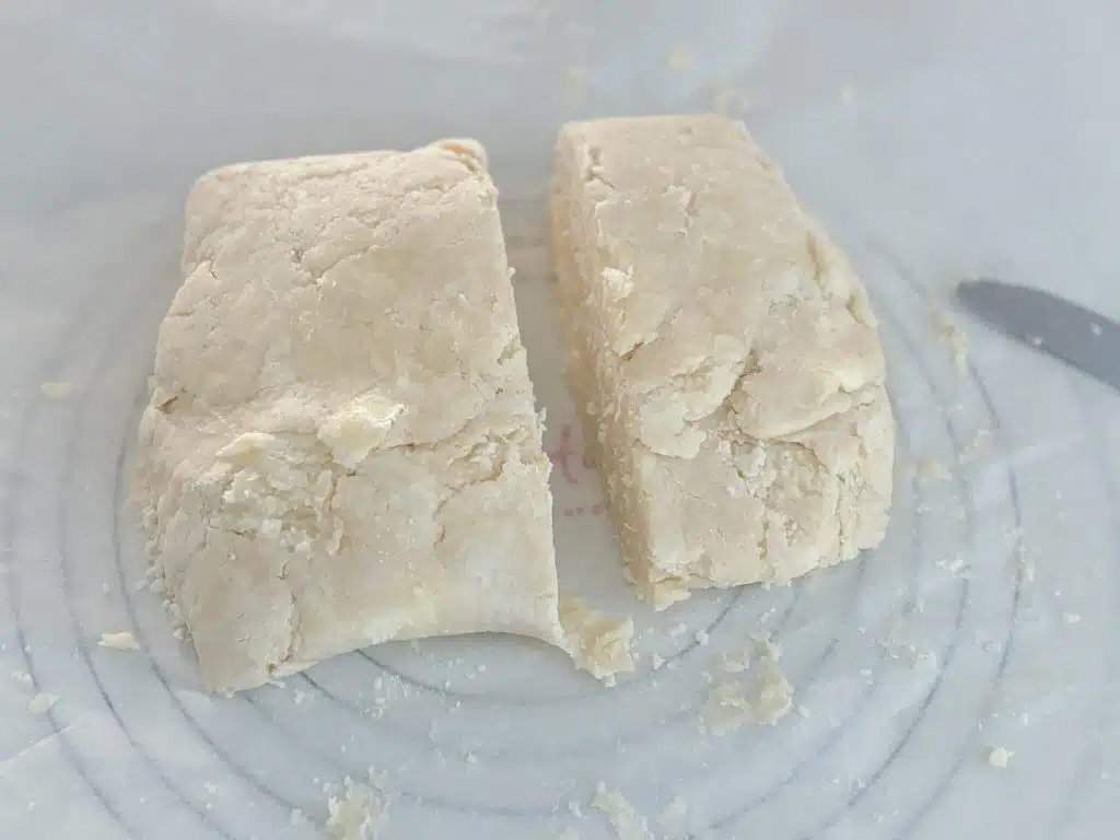 Pie crust dough on parchment paper on top of pastry mat with printed circles. Dough is cut into two pieces, with one about 60% and the other 40% of the total crust.