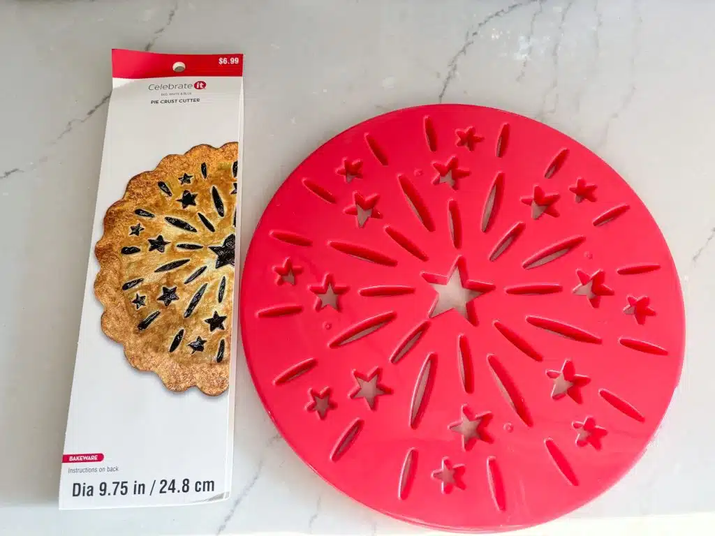 red plastic pie crust stencil with starburst design next to product sleeve with photo of baked pie on it