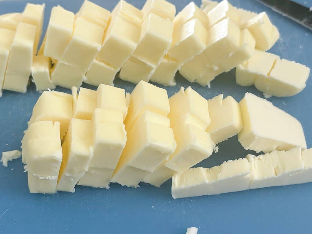 2 sticks of butter cut into cubes on blue cutting board

