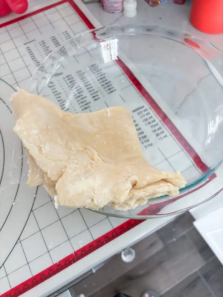 Pie crust folded into fourths and centered in glass pie plate on top of marked pastry mat.