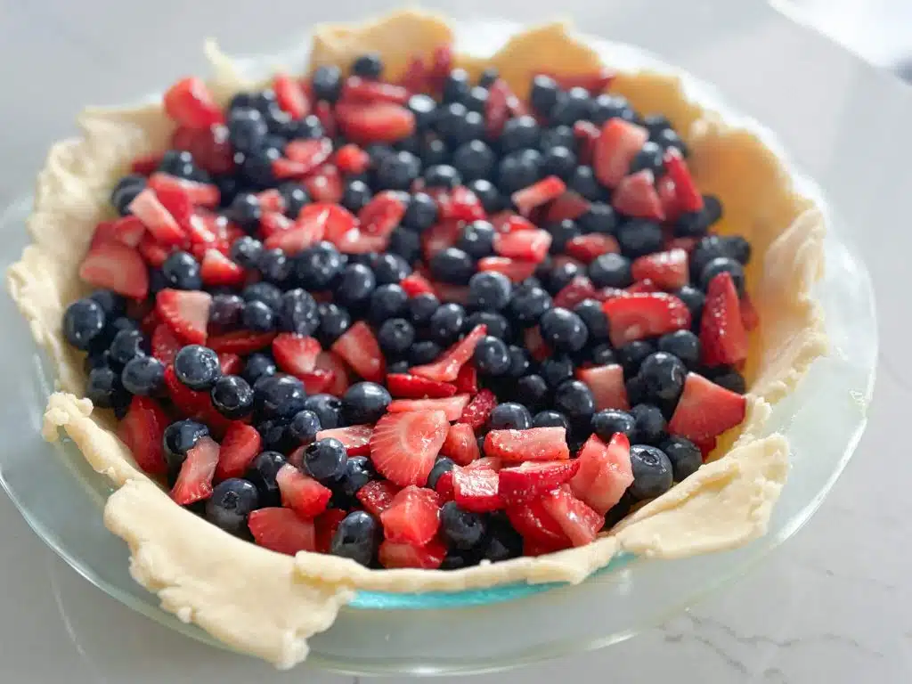 Strawberry and blueberry filling in bottom crust in glass pie plate