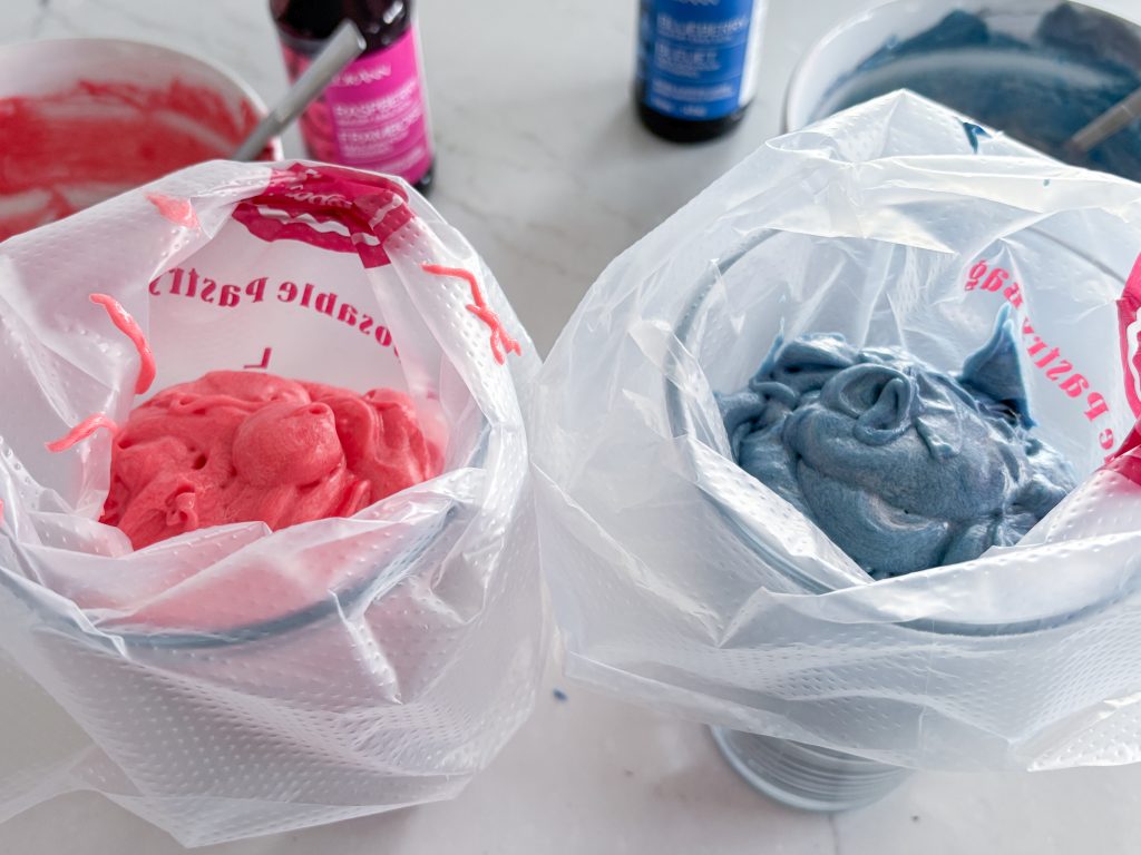 piping bags with red and blue batter in front of bottles of raspberry and blueberry emulsions