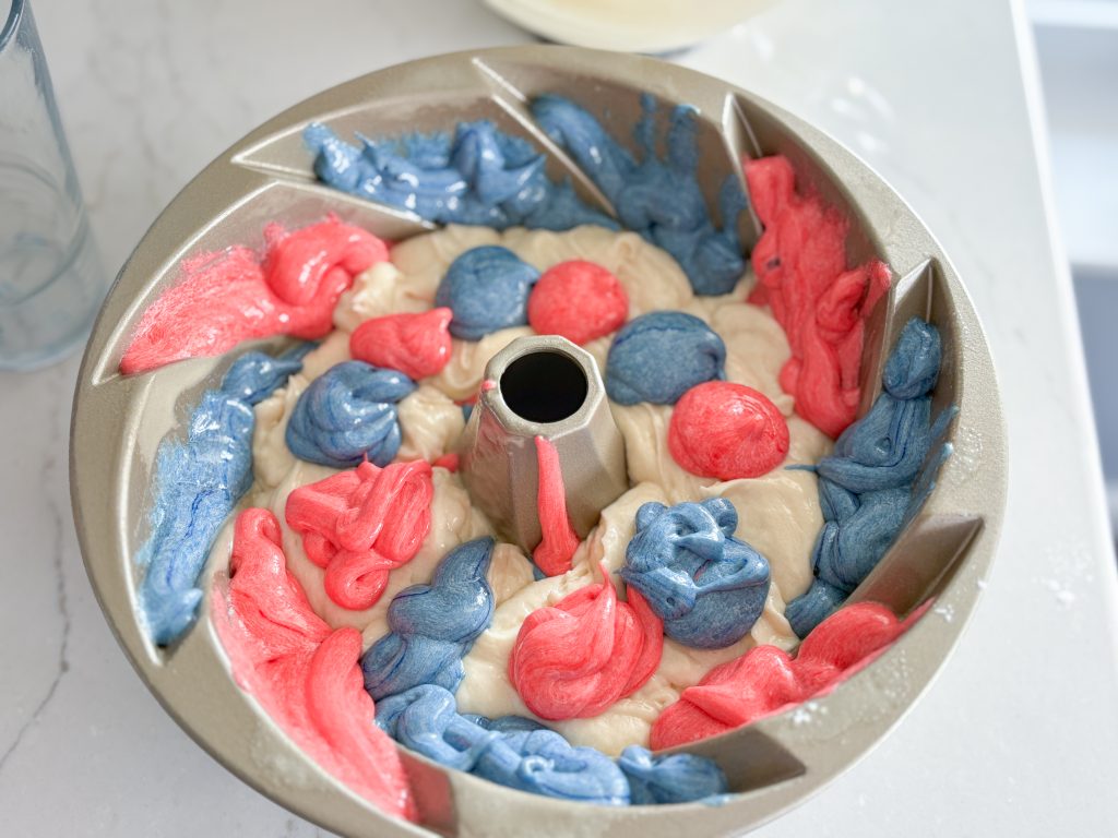 Heritage Bundt pan with layer of white batter on top of red and blue swirls of batter, topped with dollops of red and blue batter