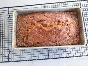 Loaf of cranberry pumpkin bread in aluminum pan cooling on rack