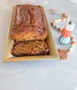 Cranberry pumpkin loaf on gold platter with 2 slices cut, next to stack of white, orange and blue pumpkins and beads