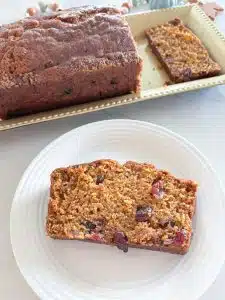 Loaf of cranberry pumpkin bread on gold platter with one slice on white plate