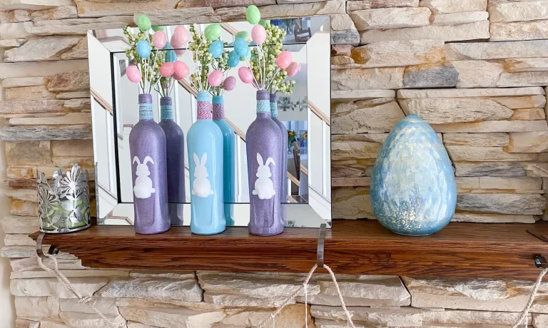 2 purple & 1 aqua bottle with white bunny silhouette labels, cotton ball tails, pink & aqua twine on bottle necks, glitter egg and green berry sprays on mantel with aqua glass egg