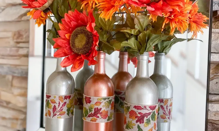 Two caramel latte spray painted bottles surrounding one candy corn spray painted bottle, decorated with fall ribbon and rust sunflowers and mums, on fireplace mantel in front of mirror